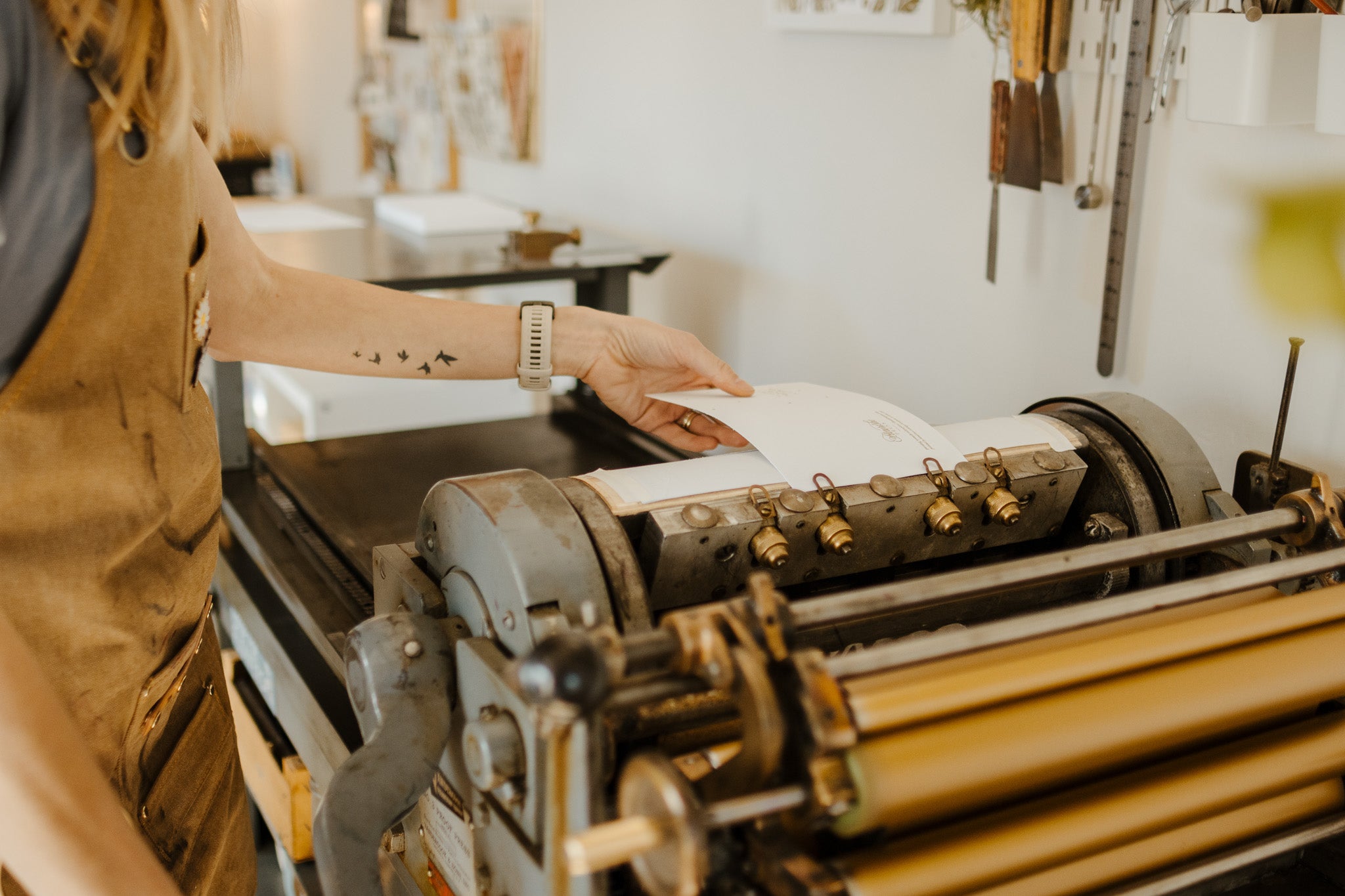 A graphic designer and letterpress artist printing letterpress art prints on a Vandercook #3 proof letterpress built around 1938 in a sunny Orem, Utah design studio
